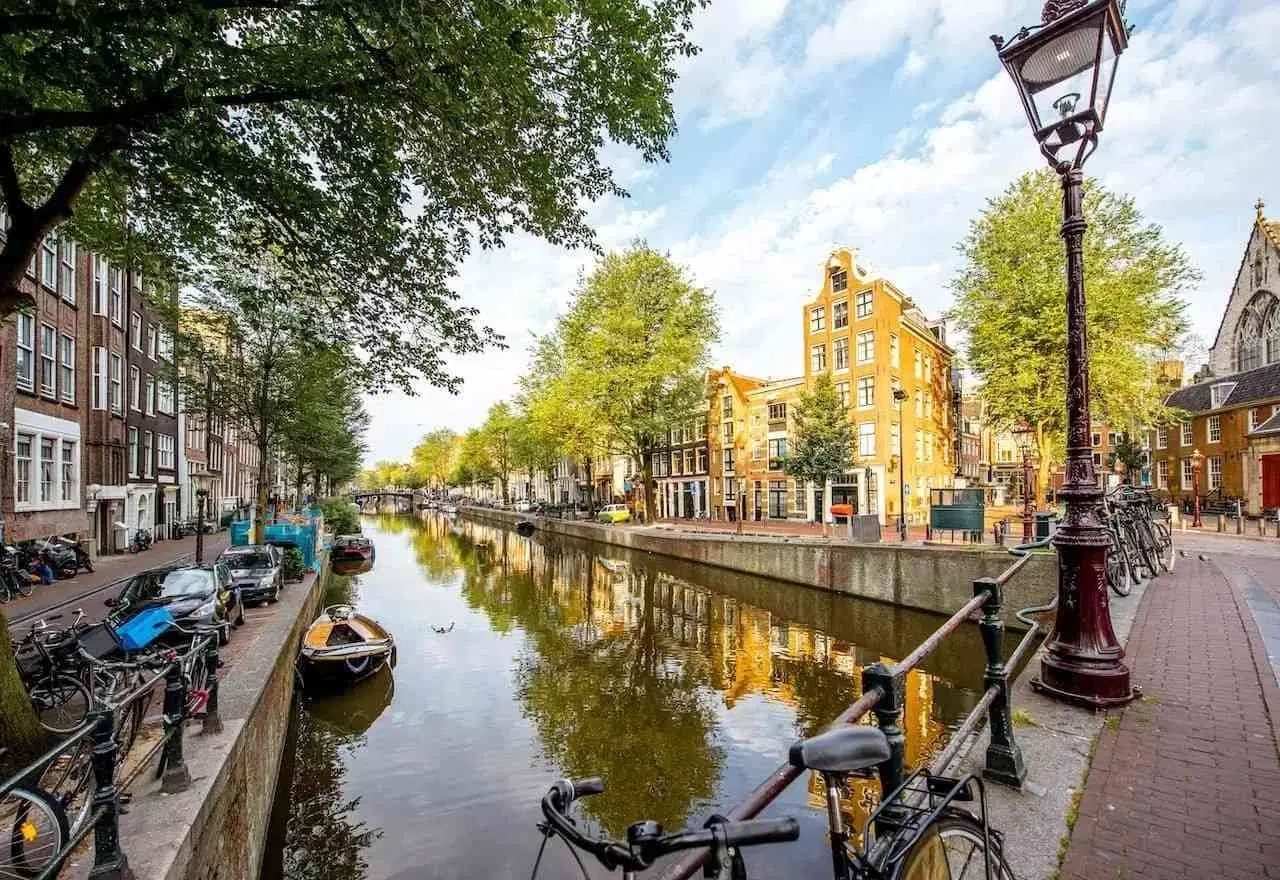 Canal in Amsterdam lined with historic buildings, bicycles, trees, and boats.