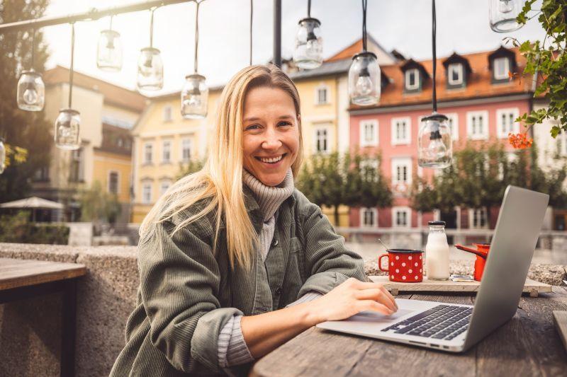 Smiling woman working on a laptop at an outdoor café.