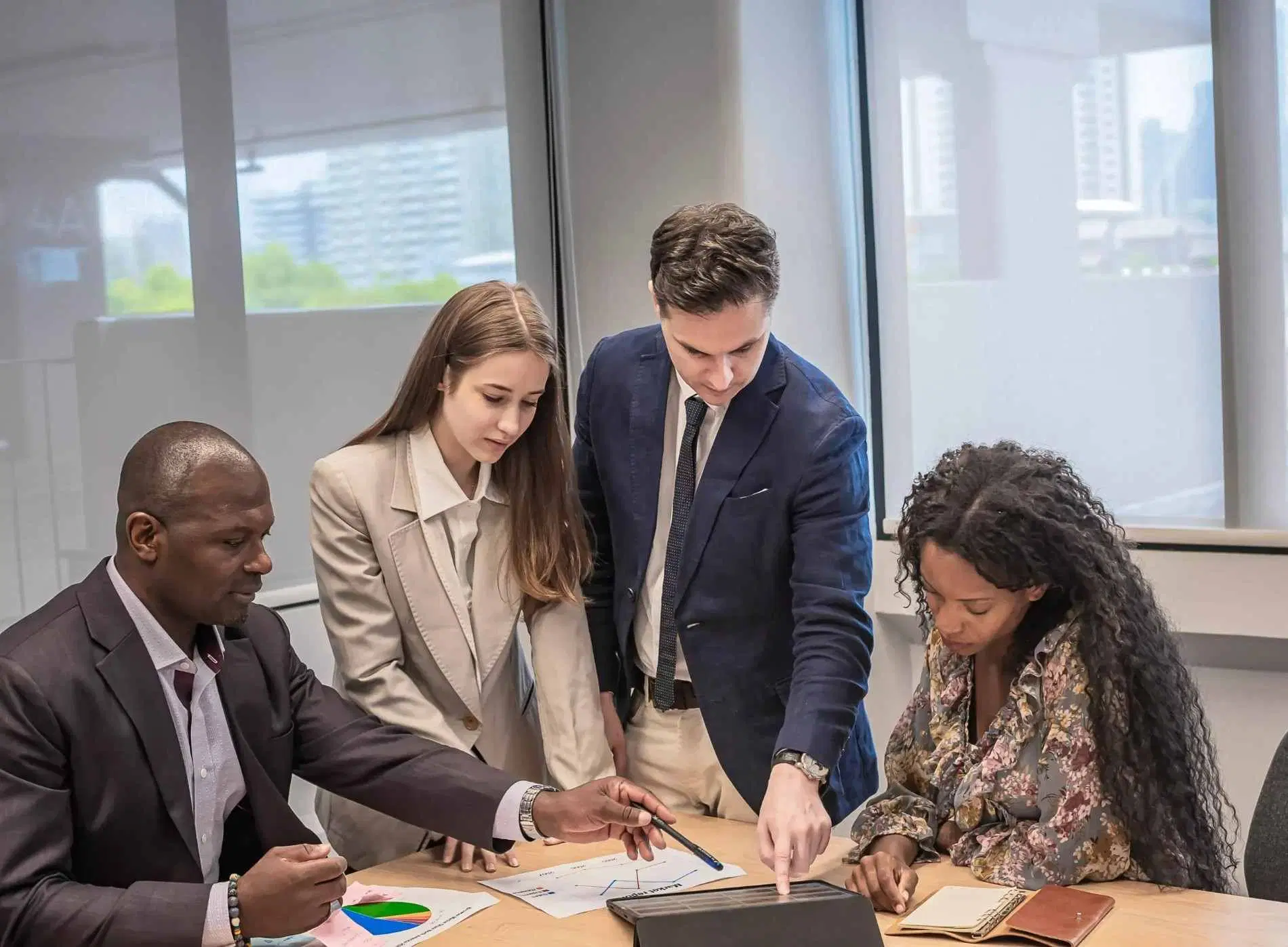 Four business professionals discussing data on a tablet during a meeting.