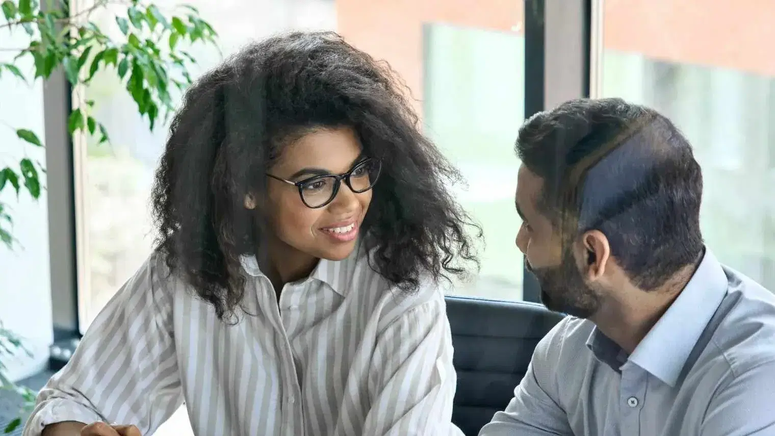 Two business professionals discussing work together at a table in a modern office.