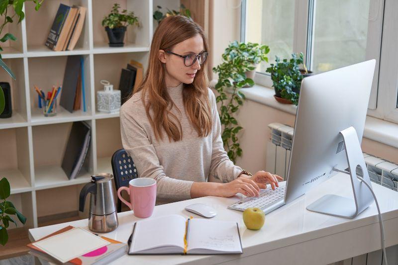 Freelancer working on a computer in a bright home office surrounded by plants and books.