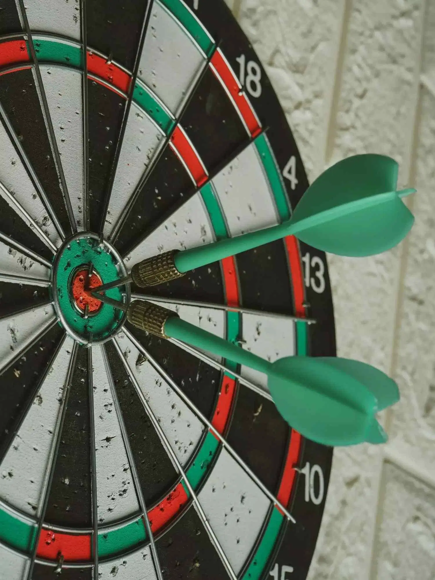 Two green darts hitting the bullseye of a dartboard.