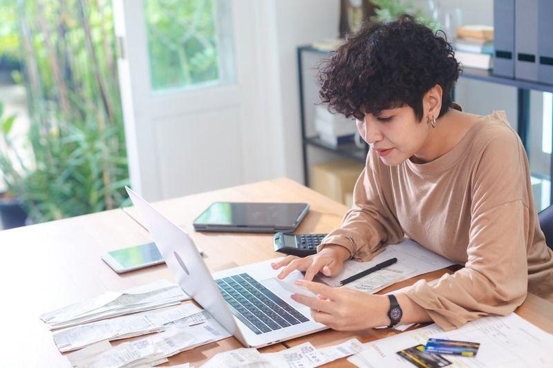 Freelancer managing expenses on a laptop with receipts, financial documents, a calculator, and credit cards