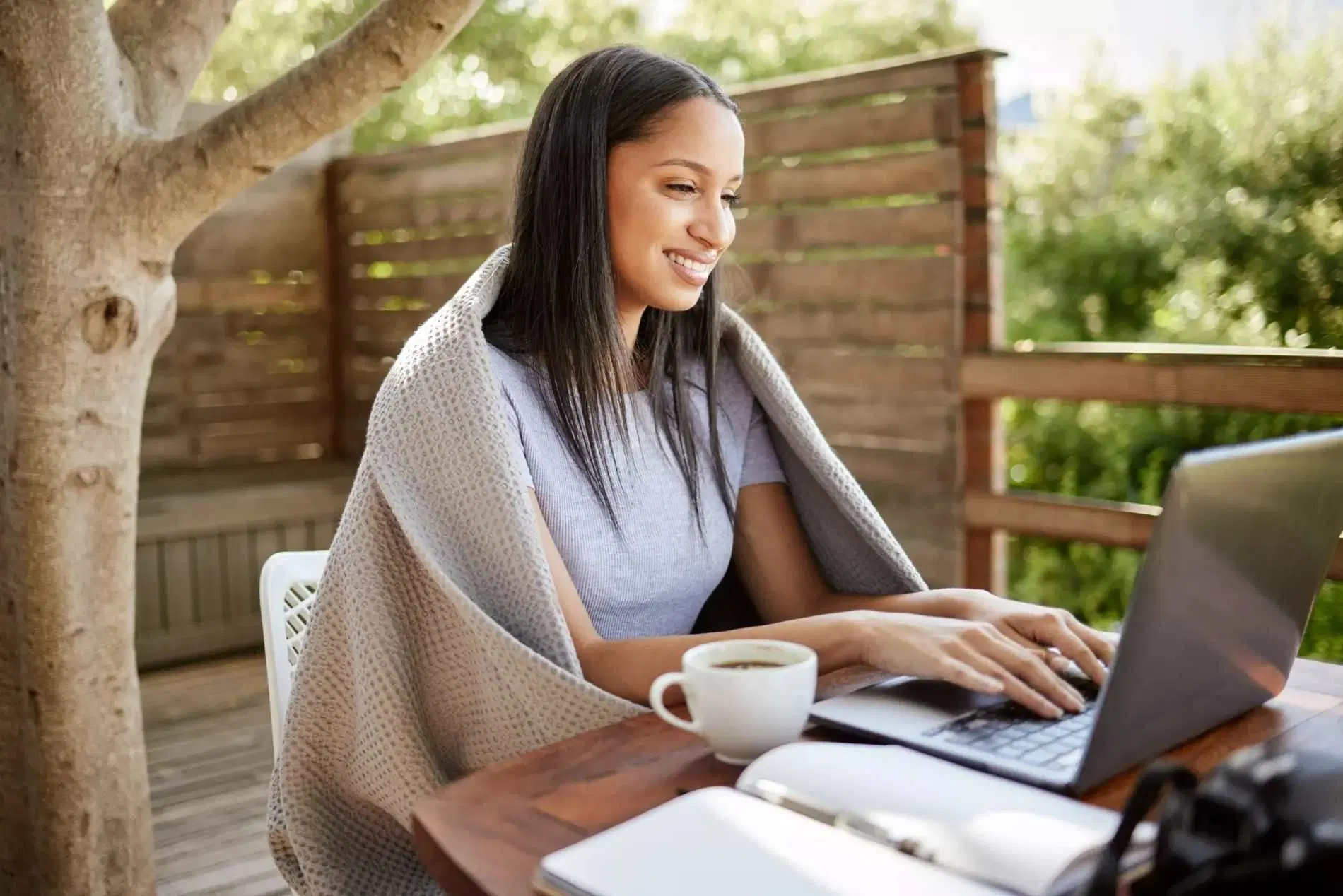 Woman working on a laptop outdoors with a cup of coffee.