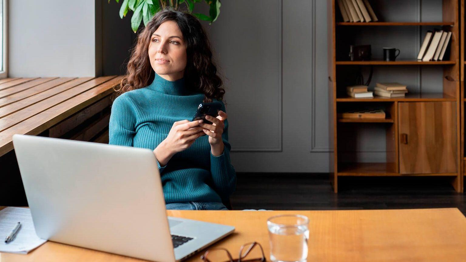 A freelancer is looking at the horizon while she works. She's holding a mobile phone in her hand.