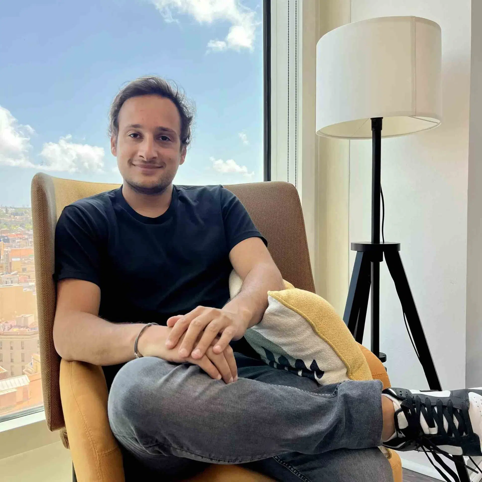 Nathan sitting in an armchair beside a large window with a city view.