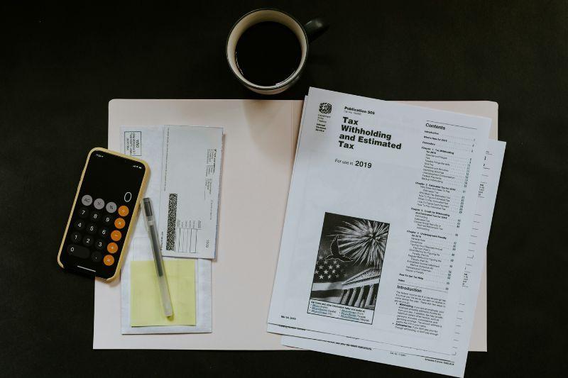 Illustrating umbrella company expenses with tax documents, calculator, envelopes, and coffee.