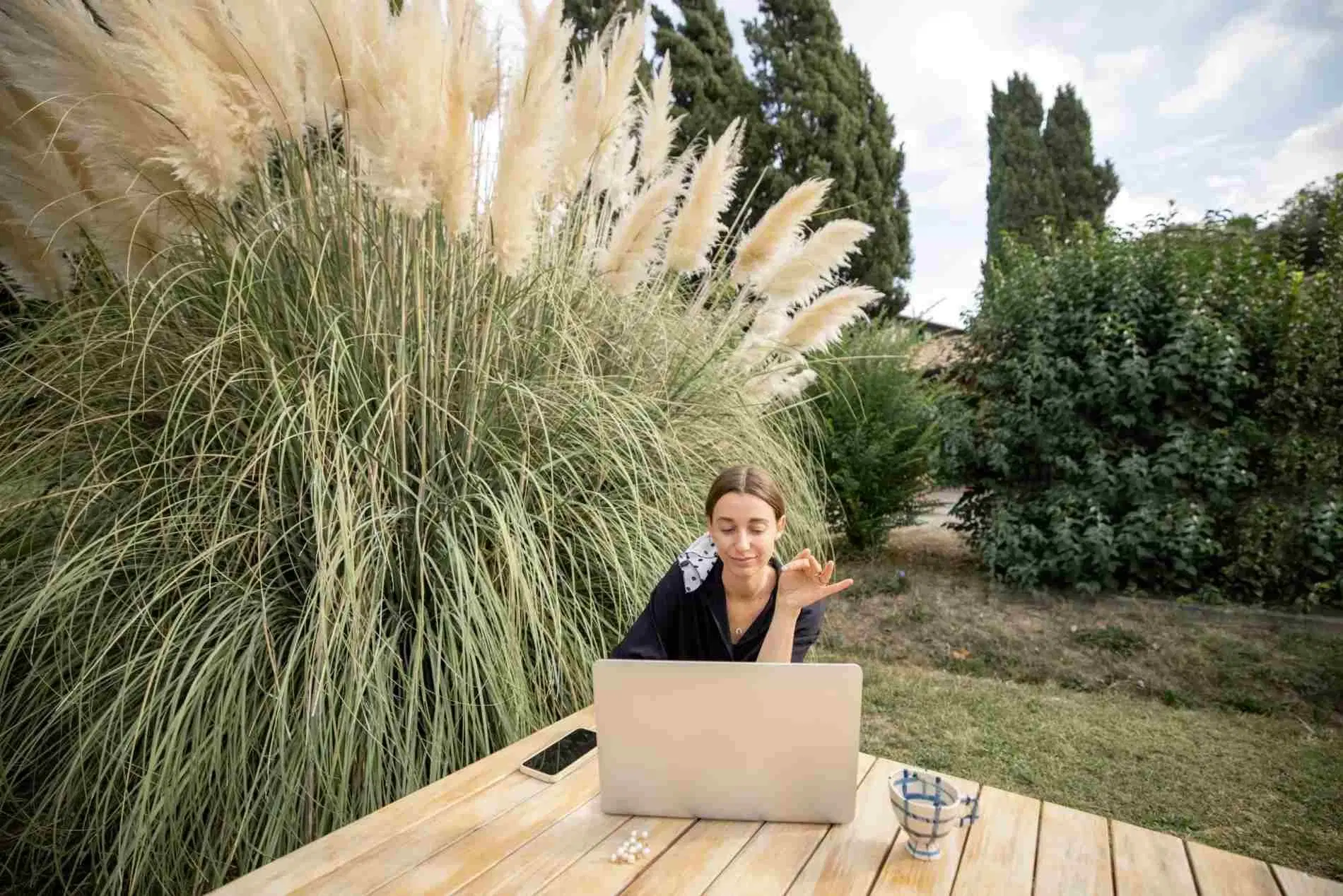 Freelancer having a video call on her laptop while working outdoors in a garden.
