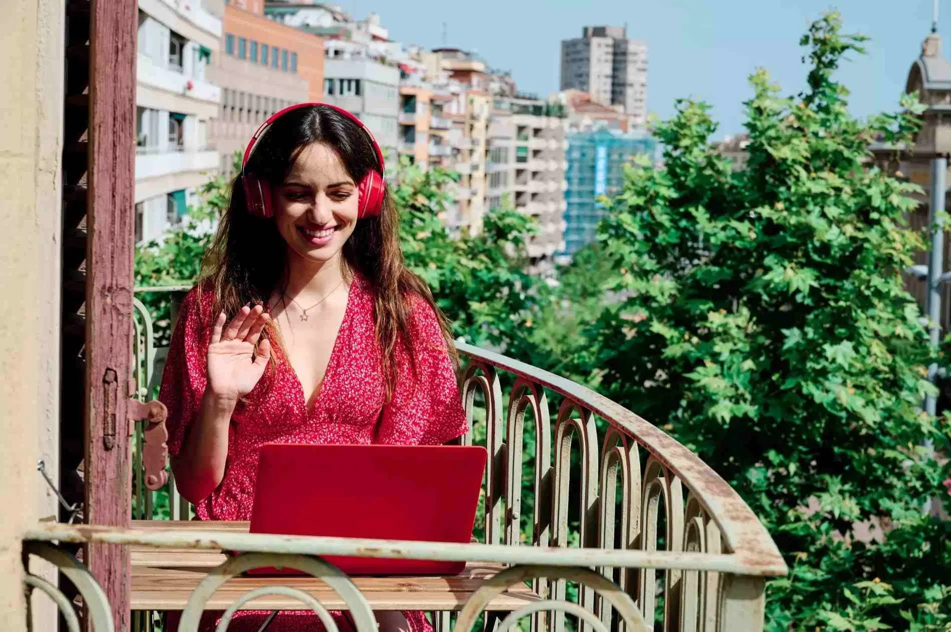 Woman smiling during a video call on her laptop from a sunny balcony.